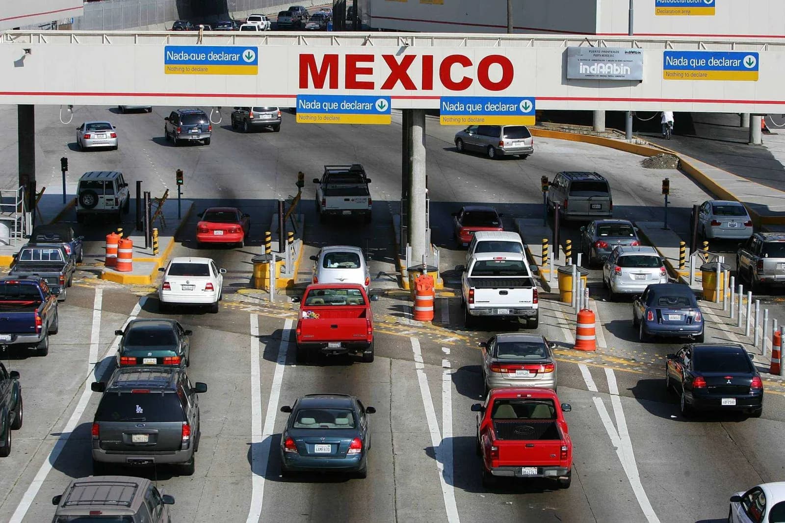 Lines of cars at a border crossing under a large MEXICO sign