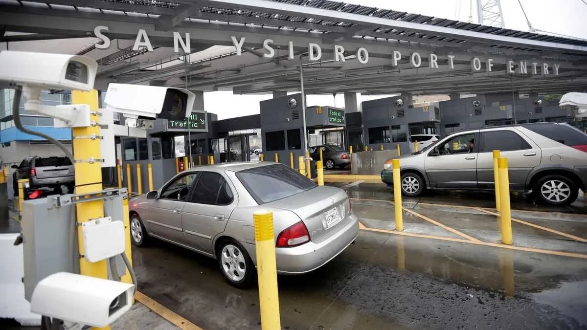 San Ysidro Port of Entry sign above vehicle inspection lanes with cars queued — best time to cross from Tijuana to San Diego