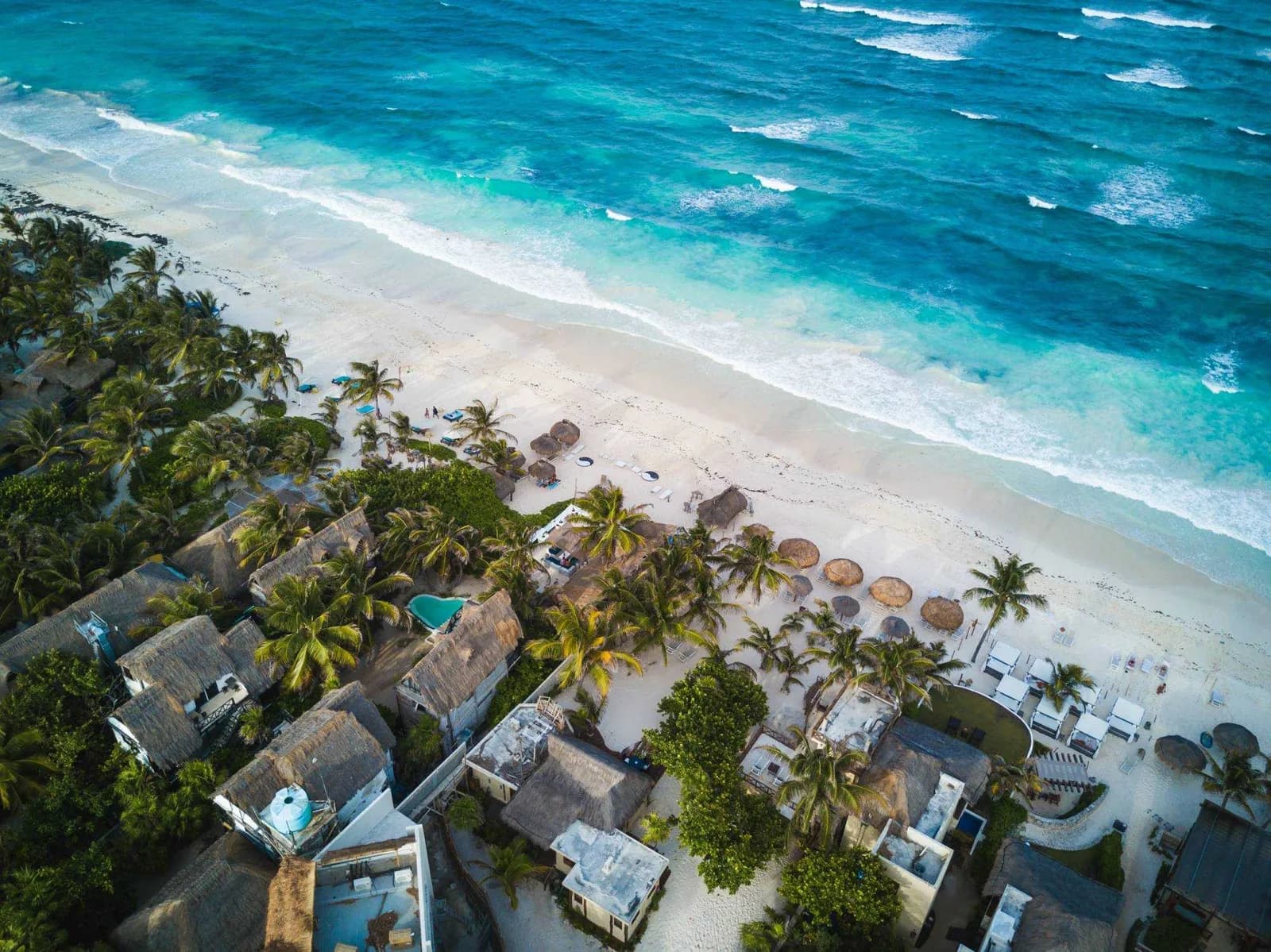 Aerial view of Mexican beachfront homes with palapa roofs beside turquoise water — average cost of homeowners insurance in Mexico